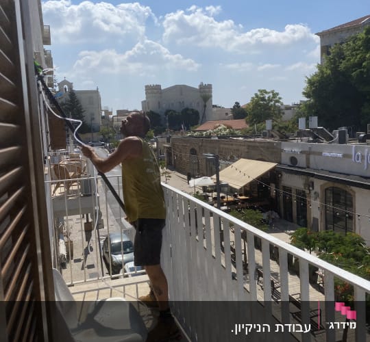 אדם מנקה חלון עם צינור מים במרפסת
